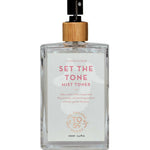 A clear spray bottle of The Organic Skin Co Set The Tone Mist Toner 100ml, topped with a wooden cap, contains hydrating rose water—an organic facial mist ideal for refreshing and balancing your skin.