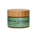The Organic Skin Co Soothe Operator Balm 50ml comes in a green jar with a wooden lid, featuring calming turmeric and calendula. This organic, nourishing, and balancing balm is ideal for sensitive skin.