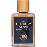 A 30ml bottle of The Organic Skin Co The Only Glow Tinted Face Oil in Light, with a wooden cap and black label with gold text, gives a luminous dewy finish using organic ingredients.