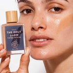 A woman with radiant skin holds The Organic Skin Co The Only Glow Tinted Face Oil Medium 30ml by her face, showcasing its warm tint and wooden cap—perfect for a luminous look with organic makeup.