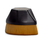Three Warriors Beauty Buff Brush with a short, faceted black grip above a broad, dense row of golden-brown bristles.