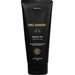 A black tube labeled "Three Warriors Gradual Tan 150g," a certified organic self-tanner made in Australia with natural DHA and Tasmanian olive oil for hydration, featuring gold and white text and symbols.