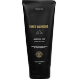 A black tube labeled "Three Warriors Gradual Tan 150g," a certified organic self-tanner made in Australia with natural DHA and Tasmanian olive oil for hydration, featuring gold and white text and symbols.
