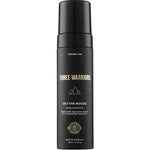 A black bottle of Three Warriors Self Tanning Mousse 150ml with gold and white text and a pump dispenser. This organic self-tan uses natural DHA and Tasmanian olive oil for a flawless Australian glow.