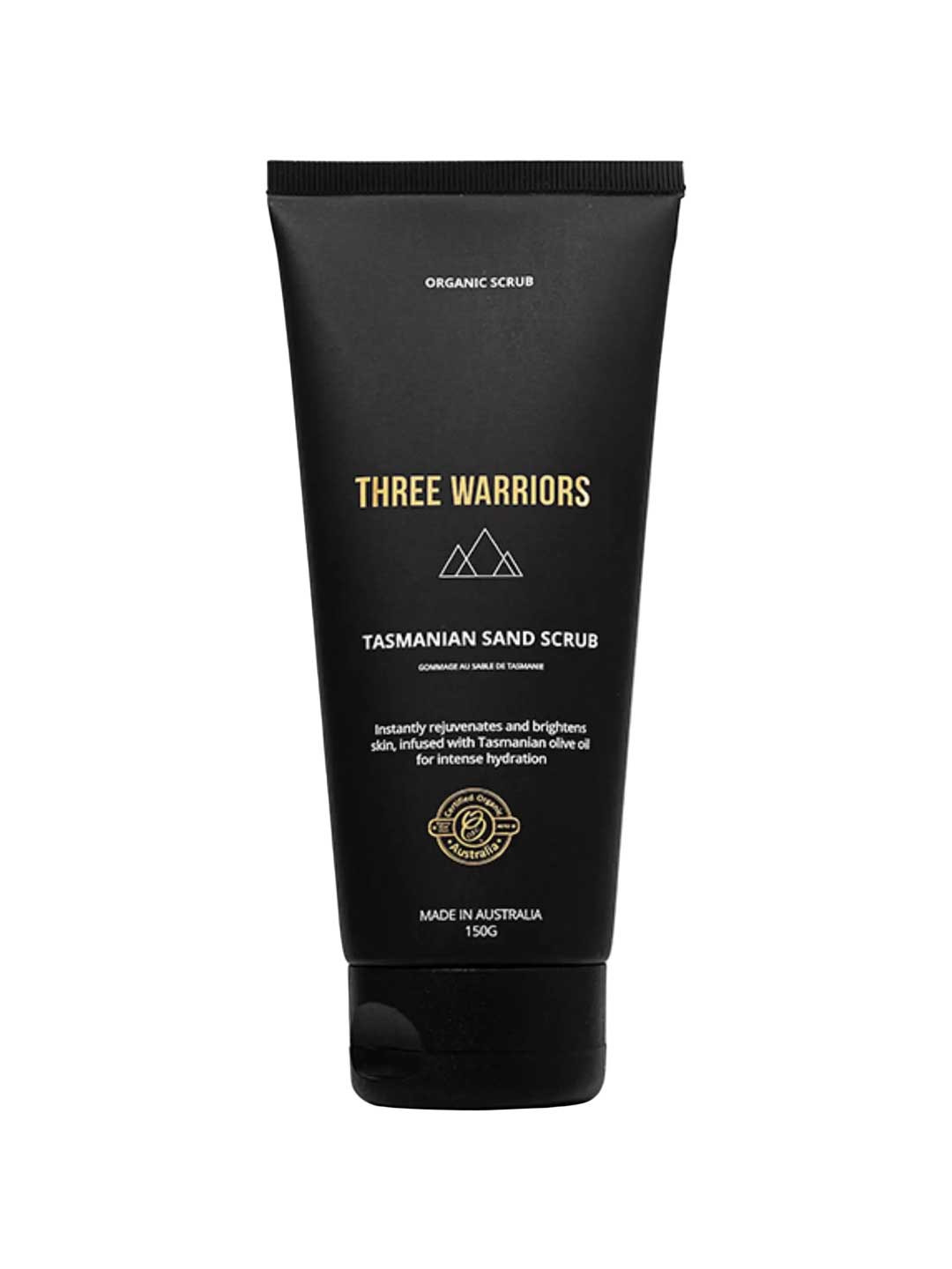 A black tube labeled Three Warriors Tasmanian Sand Scrub 150g features gold and white text, a mountain logo, and highlights its use as an organic exfoliant for intense hydration and preparing skin for self-tanning.