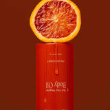 A halved blood orange sits on an upside-down Tuttofare Not Your Regular Body Oil 200ml bottle with orange liquid dripping down, set against a deep red background, emphasizing this luxurious natural moisturizer.