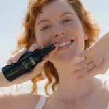 Woman misting her face with Tuttofare Naturally Active Face Mist under a blue sky