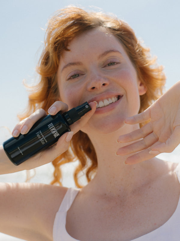 Woman misting her face with Tuttofare Naturally Active Face Mist under a blue sky