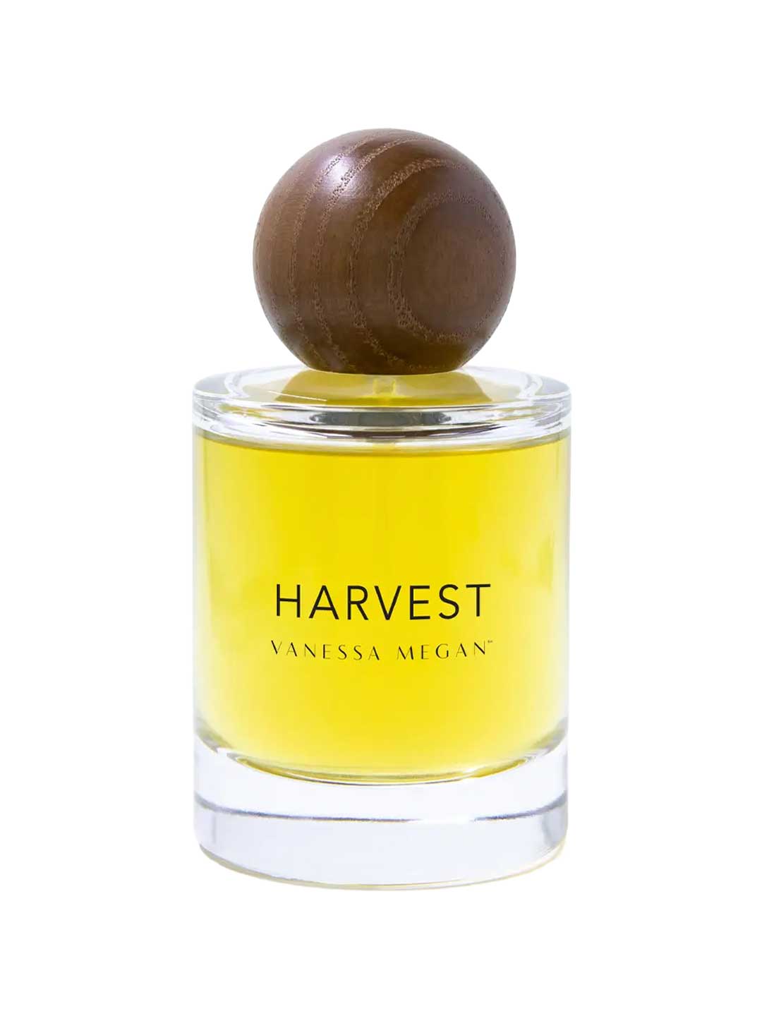 A clear glass bottle with yellow liquid, labeled Vanessa Megan Harvest 100% Natural Eau de Parfum 50ml, features a large round wooden cap—an elegant, natural fragrance from Vanessa Megan.