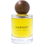 A clear glass bottle with yellow liquid, labeled Vanessa Megan Harvest 100% Natural Eau de Parfum 50ml, features a large round wooden cap—an elegant, natural fragrance from Vanessa Megan.