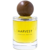 A clear glass bottle with yellow liquid, labeled Vanessa Megan Harvest 100% Natural Eau de Parfum 50ml, features a large round wooden cap—an elegant, natural fragrance from Vanessa Megan.