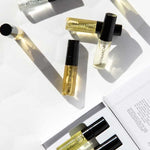 A flat lay of Vanessa Megan 100% Natural Mini Eau de Parfum Collection (6 x 3ml) bottles—AETHER, HARVEST, WILD INDIGO, MONARCH, and LIQUOR—shown beside the open box with more plant-based fragrance vials and a booklet.