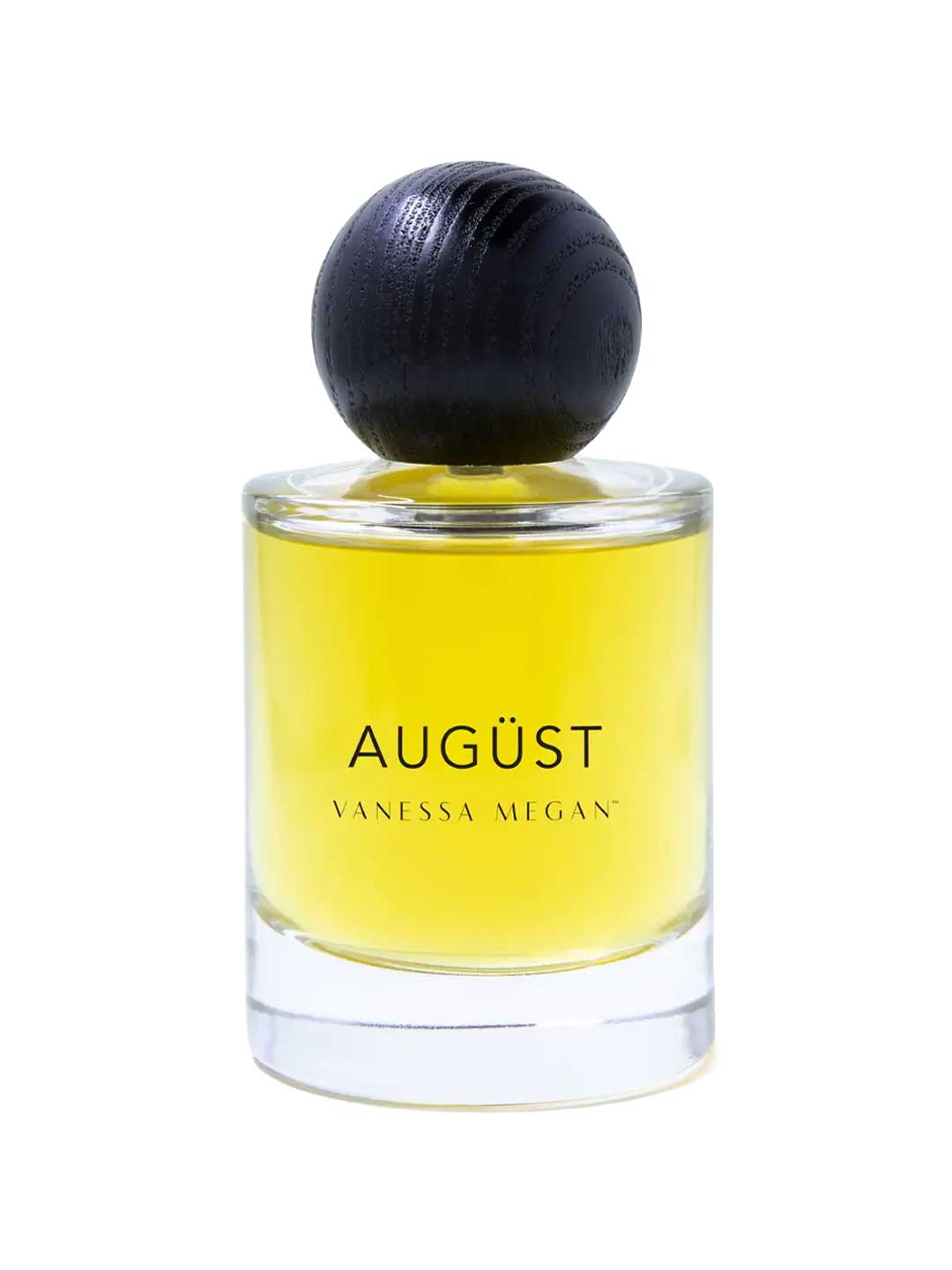 The Vanessa Megan Augüst 100% Natural Eau de Parfum (50ml) is a clear glass bottle with yellow liquid, a large round dark cap, and contains botanical perfume inspired by Australian bush scents.