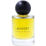 The Vanessa Megan Augüst 100% Natural Eau de Parfum (50ml) is a clear glass bottle with yellow liquid, a large round dark cap, and contains botanical perfume inspired by Australian bush scents.