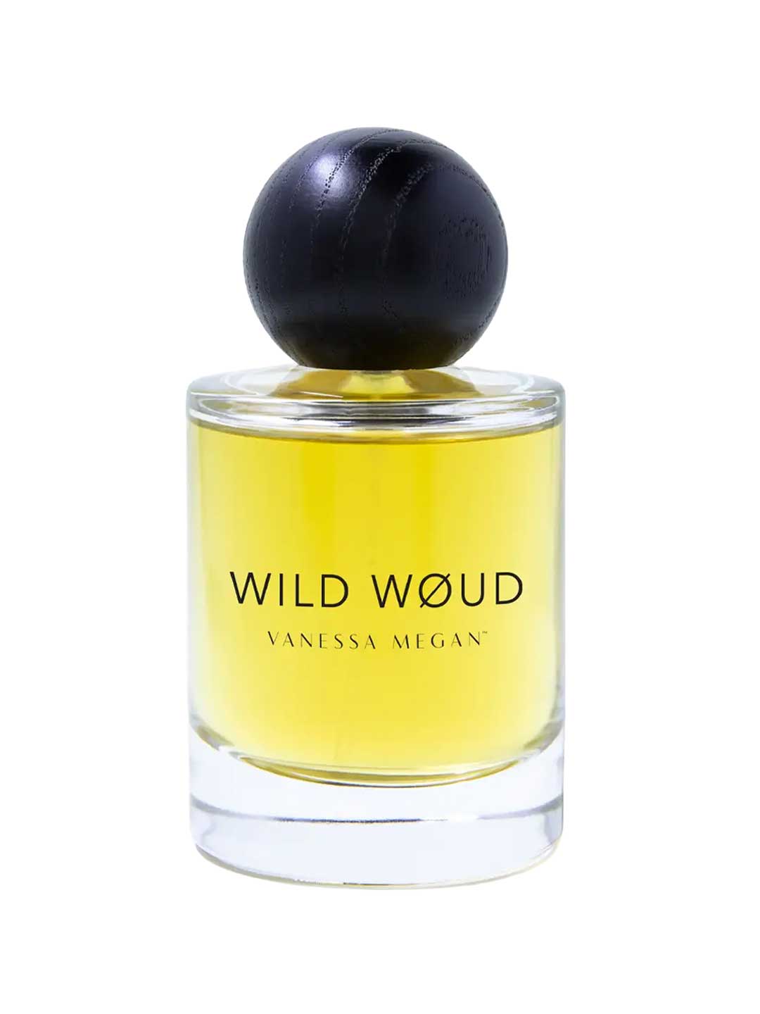 A clear glass bottle of Vanessa Megan Wild Wøud 100% Natural Eau de Parfum 50ml, with yellow liquid and a round black cap, is labeled Vanessa Megan and stands against a white background.