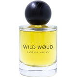 A clear glass bottle of Vanessa Megan Wild Wøud 100% Natural Eau de Parfum 50ml, with yellow liquid and a round black cap, is labeled Vanessa Megan and stands against a white background.