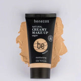A tube of Benecos Natural Creamy Makeup 30ml in vanilla lies on a foundation smear, showcasing features like vegan makeup, moisturising foundation, and a new formula highlighted on the packaging.