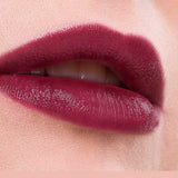 Close-up of lips wearing Benecos MAT Lipsticks 4.5 in a berry shade with a natural matte finish, slightly parted to reveal teeth. Pale pink skin and background. Text below reads "Very Berry.