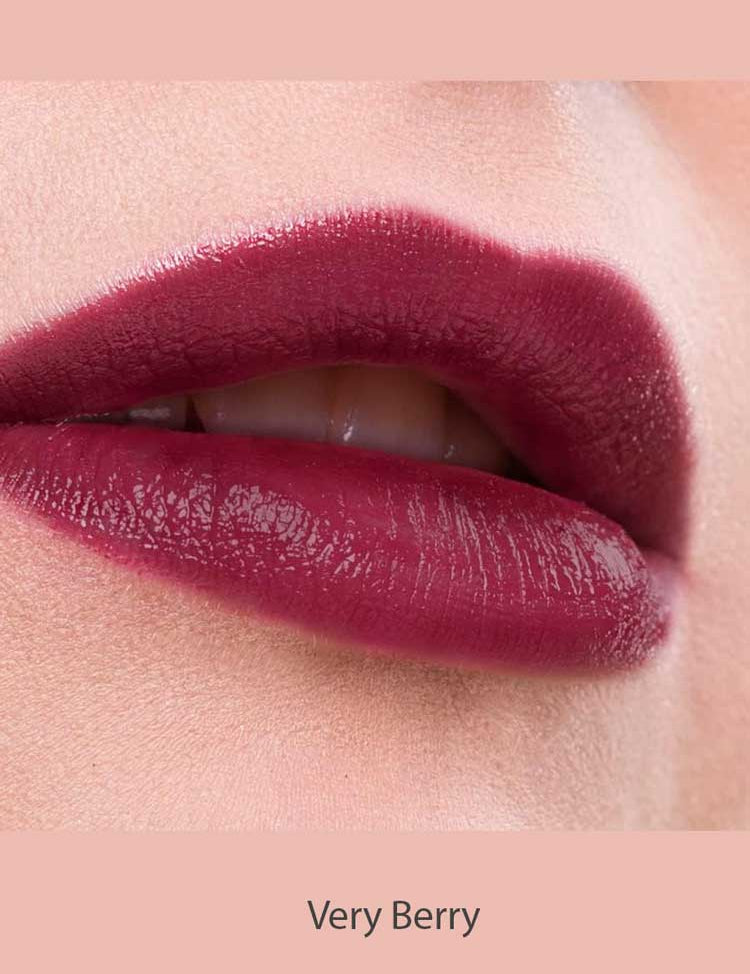 Close-up of lips wearing Benecos MAT Lipsticks 4.5 in a berry shade with a natural matte finish, slightly parted to reveal teeth. Pale pink skin and background. Text below reads "Very Berry.