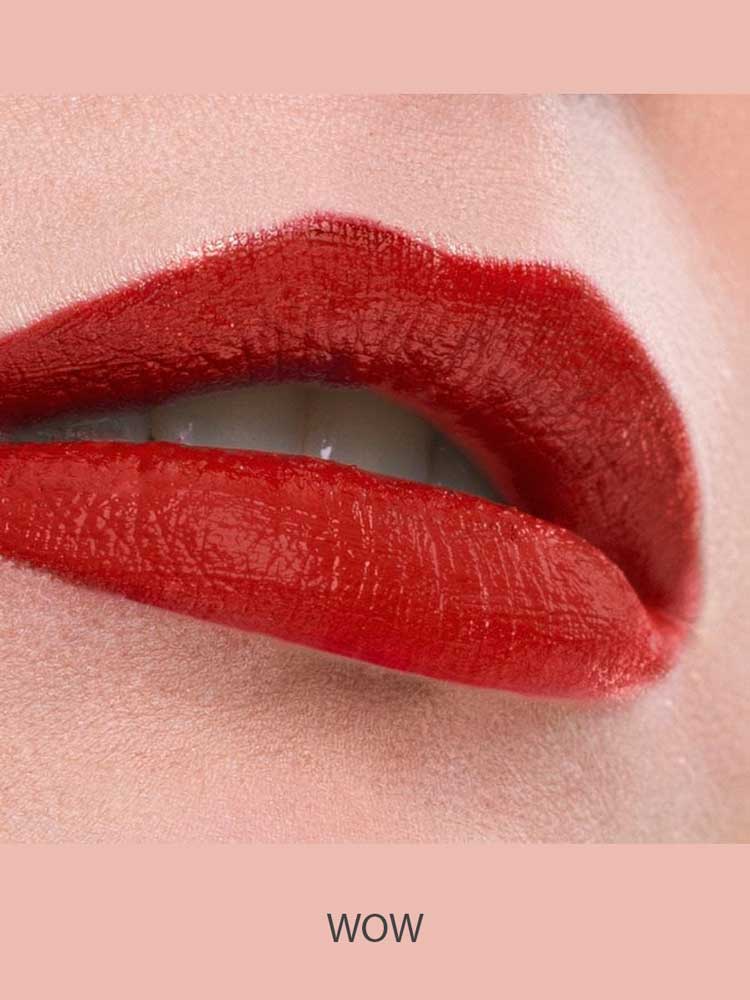 Close-up of lips wearing Benecos MAT Lipsticks 4.5 in vibrant, long-lasting glossy red, slightly parted to reveal white teeth against a soft pink background. The word WOW appears below the image.