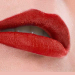 Close-up of lips wearing Benecos MAT Lipsticks 4.5 in vibrant, long-lasting glossy red, slightly parted to reveal white teeth against a soft pink background. The word WOW appears below the image.