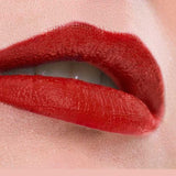 Close-up of lips wearing Benecos MAT Lipsticks 4.5 in vibrant, long-lasting glossy red, slightly parted to reveal white teeth against a soft pink background. The word WOW appears below the image.
