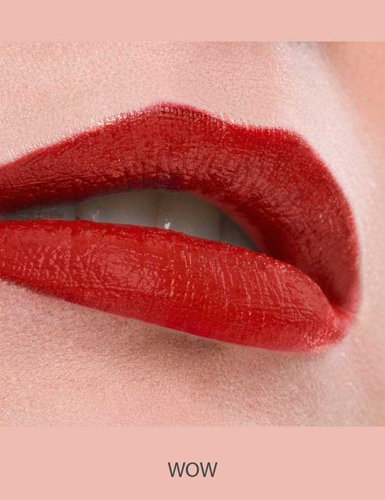 Close-up of lips wearing Benecos MAT Lipsticks 4.5 in vibrant, long-lasting glossy red, slightly parted to reveal white teeth against a soft pink background. The word WOW appears below the image.