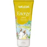 A 200ml yellow tube of Weleda Energy Shower Gel Ginger, with natural fragrance and an illustration of two people by a riverside with greenery and red flowers. The label notes energizing ginger for a refreshing shower experience.