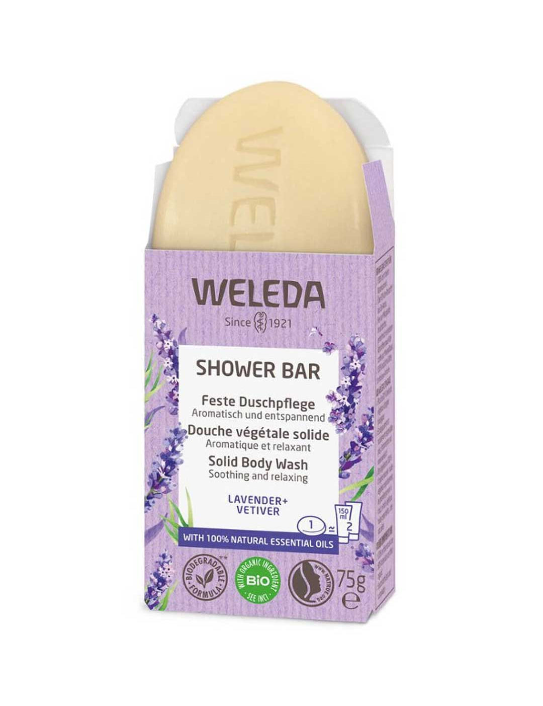 The Weleda Shower Bar Lavender & Vetiver 75g is pictured in an open lavender box with lavender illustrations, emphasizing its natural ingredients and eco certifications. The scent blends soothing lavender and vetiver.