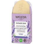 The Weleda Shower Bar Lavender & Vetiver 75g is pictured in an open lavender box with lavender illustrations, emphasizing its natural ingredients and eco certifications. The scent blends soothing lavender and vetiver.