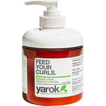 A bottle of Yarok Defining Creme on a white background, featuring a white pump dispenser, a translucent white cap, and a white label with green and black text over a reddish-brown bottle body.