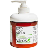 A bottle of Yarok Defining Creme on a white background, featuring a white pump dispenser, a translucent white cap, and a white label with green and black text over a reddish-brown bottle body.