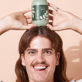 A bit Hippy Face and Body Cleanser balanced above a smiling man's head