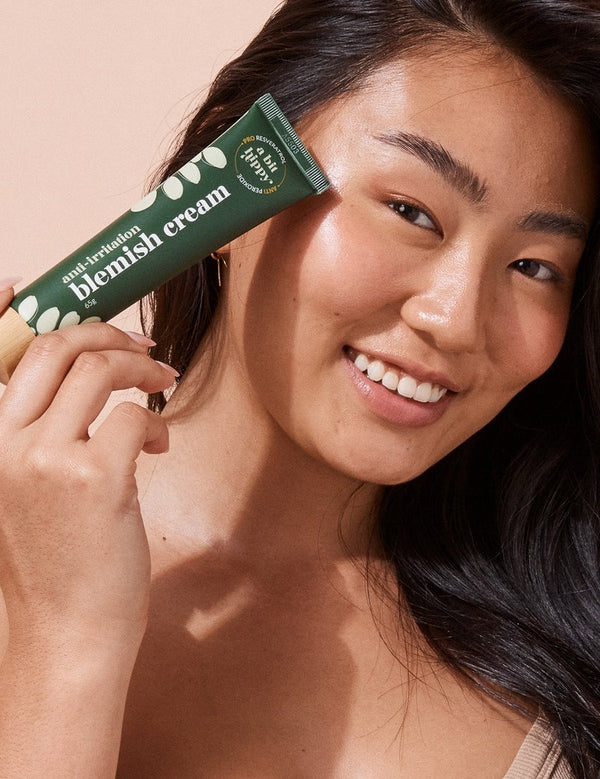 A bit Hippy Blemish Cream held beside a woman's face