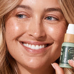 A bit Hippy Day Serum held beside a smiling woman's face