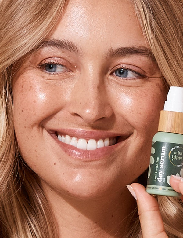 A bit Hippy Day Serum held beside a smiling woman's face