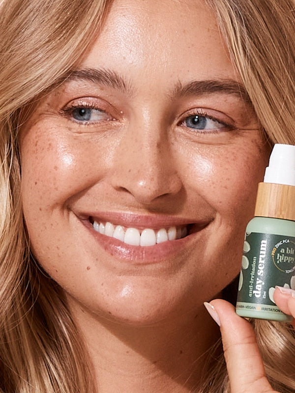 A bit Hippy Day Serum held beside a smiling woman's face