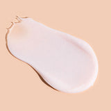 A smooth, pale pink-white swatch of A bit Hippy Night Cream on peach, shaped like a teardrop with a rounded end and a thin, slightly ragged tip.
