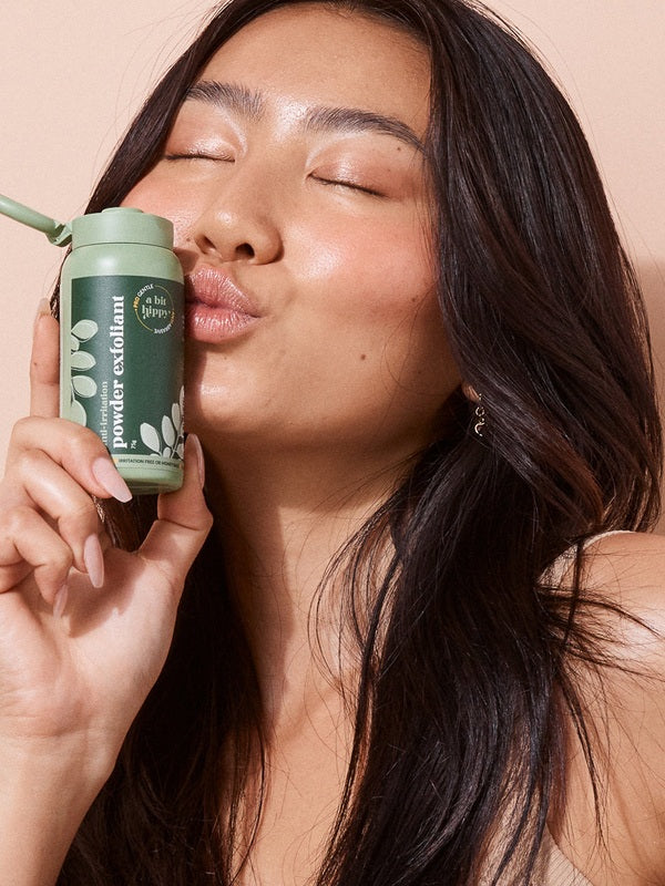 A bit Hippy Powder Exfoliant held beside a smiling woman's face