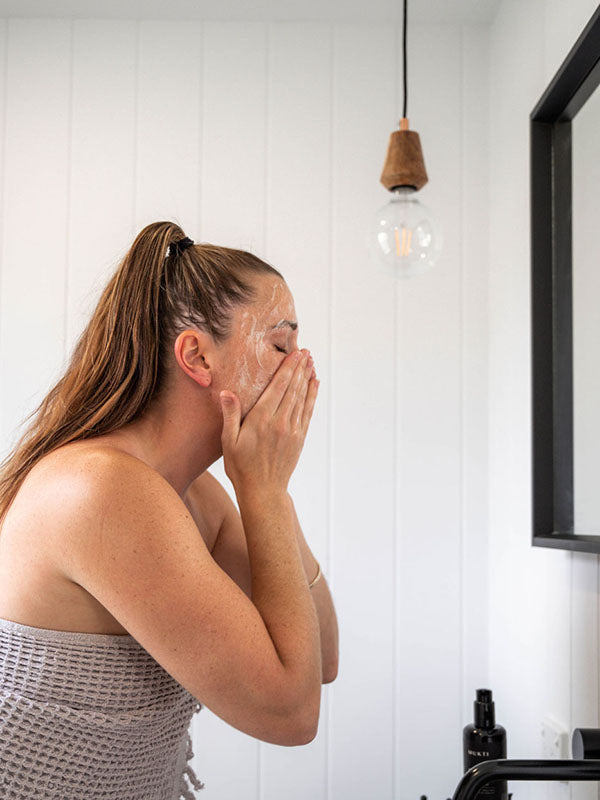 Woman washing her face at the bathroom mirror with Mukti Balancing Cleansing Gel