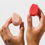 Hands holding the two Ere Perez Bio All-Beauty Sponges in peach and coral