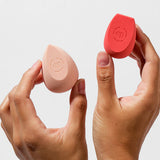 Hands holding the two Ere Perez Bio All-Beauty Sponges in peach and coral