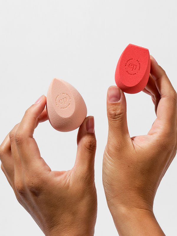 Hands holding the two Ere Perez Bio All-Beauty Sponges in peach and coral