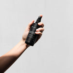 Hand holding up the Mukti Botanique Natural Deodorant Sandalwood and Sage spray bottle
