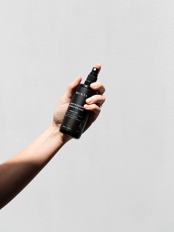 Hand holding up the Mukti Botanique Natural Deodorant Sandalwood and Sage spray bottle