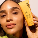 Model holding ACURE Brightening Cleansing Gel beside her face