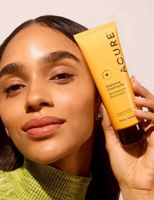 Model holding ACURE Brightening Cleansing Gel beside her face
