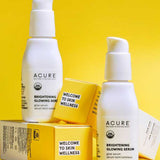 Two white bottles of Acure Brightening Glowing Serum 30ml are shown against a yellow background, each on or near a yellow “Welcome to Skin Wellness” box, spotlighting the secret to radiant skin.
