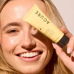 Model holding ACURE Brightening Night Cream beside her face