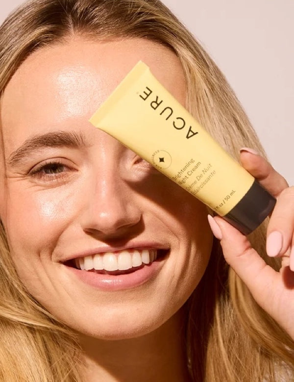Model holding ACURE Brightening Night Cream beside her face